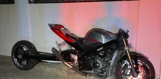 Motociclista a bay dal tras di un Suzuki Swift staciona banda robes (links) di caminda mitar riba acer